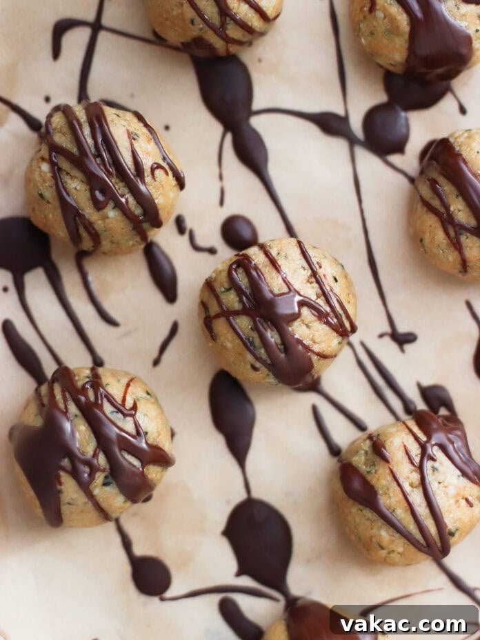No-Bake Peanut Butter Oat Flour Energy Bites 7 Round energy bites drizzled with dark chocolate are arranged on a sheet of parchment paper, with additional chocolate splatters creating a decorative pattern in the background.