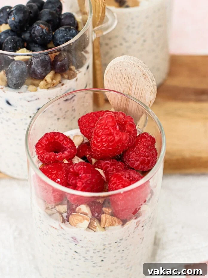 Glass cups filled with overnight oats topped with raspberries, blueberries, and chopped nuts, each with a small wooden spoon. The cups are placed on a white cloth and wooden board.
