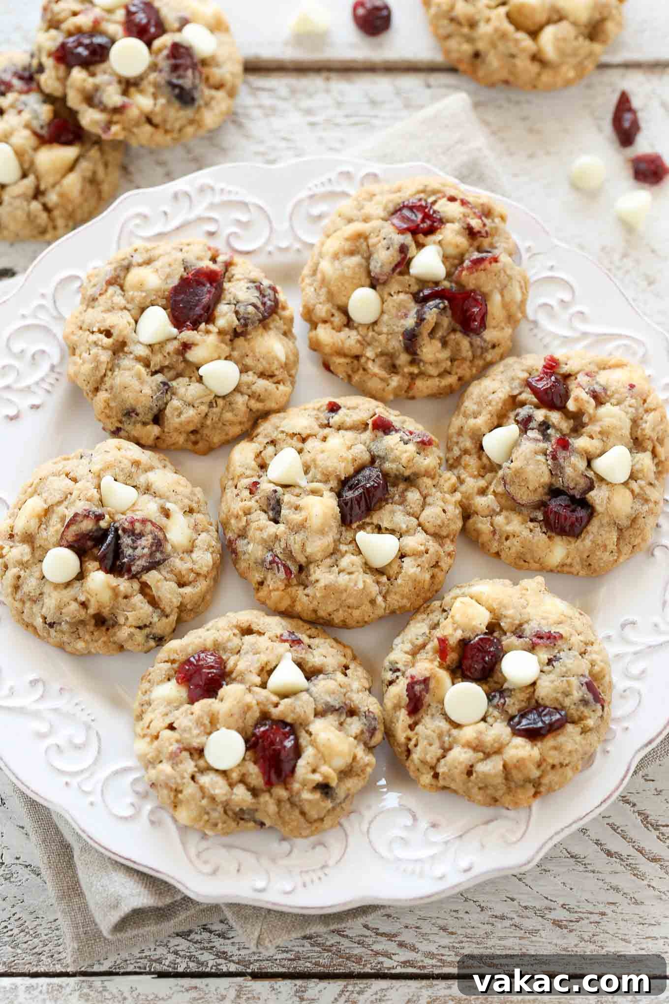 Irresistibly Soft and Chewy White Chocolate Cranberry Oatmeal Cookies 2 Overhead view of seven white chocolate oatmeal cranberry cookies on a white plate. Additional cookies rest on the counter, suggesting a freshly baked batch.