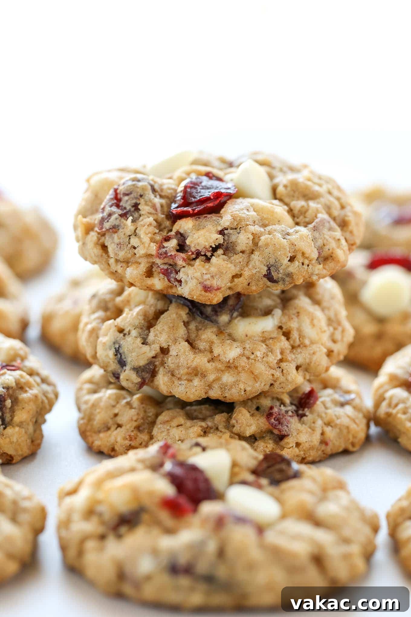 Irresistibly Soft and Chewy White Chocolate Cranberry Oatmeal Cookies 4 A stack of three white chocolate cranberry oatmeal cookies, showcasing their soft texture and visible mix-ins. Additional cookies surround the stack on a white plate.