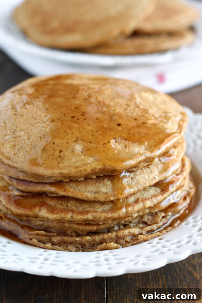 Cozy Gingerbread Pancakes 3 A tempting stack of gingerbread pancakes on a white plate, with additional fluffy pancakes blurred in the background, suggesting an abundance of deliciousness ready to be served.