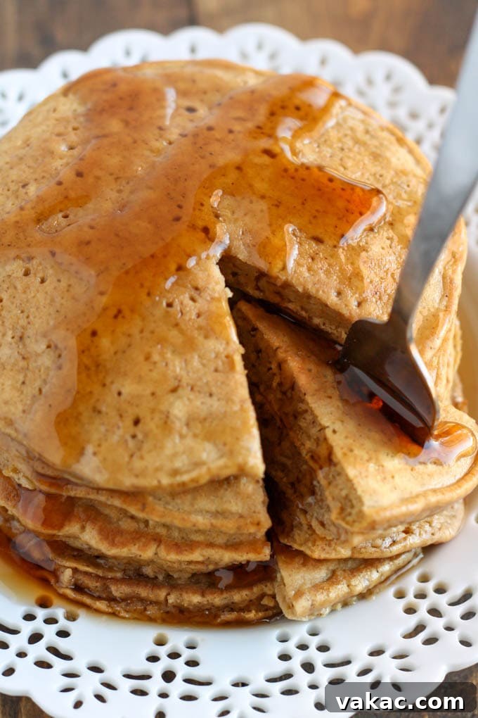 Cozy Gingerbread Pancakes 5 A close-up shot of a stack of golden-brown gingerbread pancakes, with a noticeable bite taken out, resting on a clean white plate. The soft, textured interior and inviting warmth are evident, beckoning to be enjoyed.
