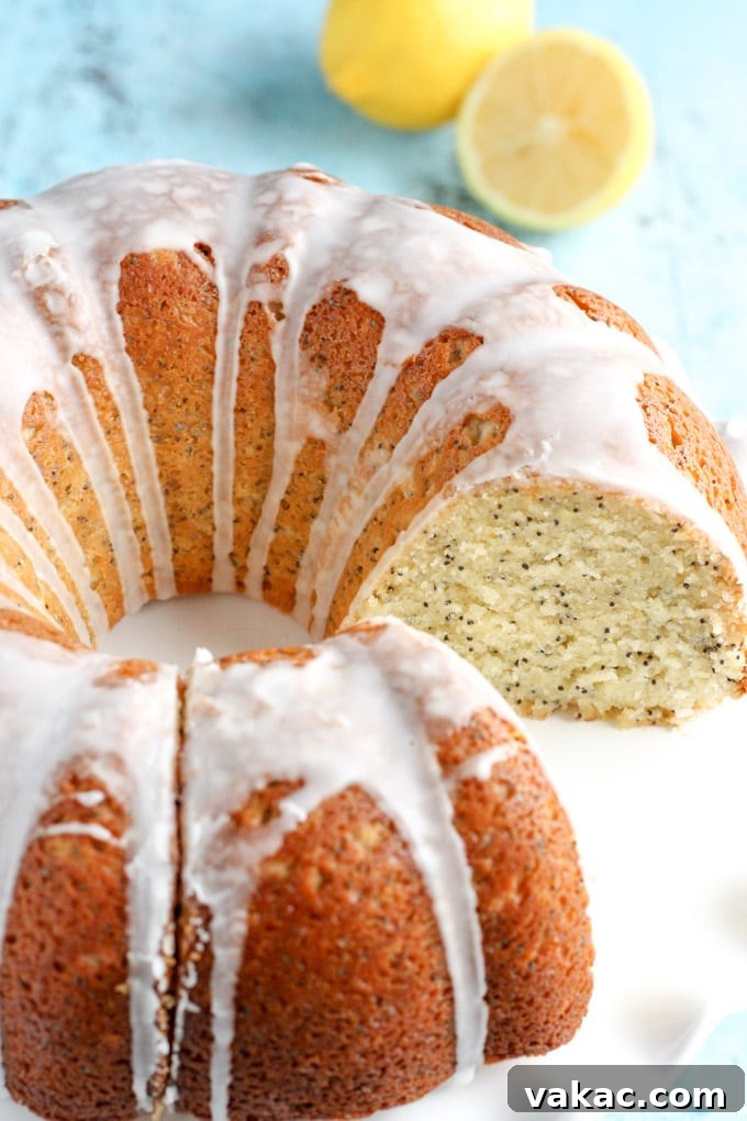 Zesty Lemon Poppy Seed Bundt Cake 3 A stunning glazed lemon bundt cake displayed on a pristine white cake stand. One perfect slice has been removed, revealing the soft, textured interior of the cake and the consistent application of the tangy lemon glaze.