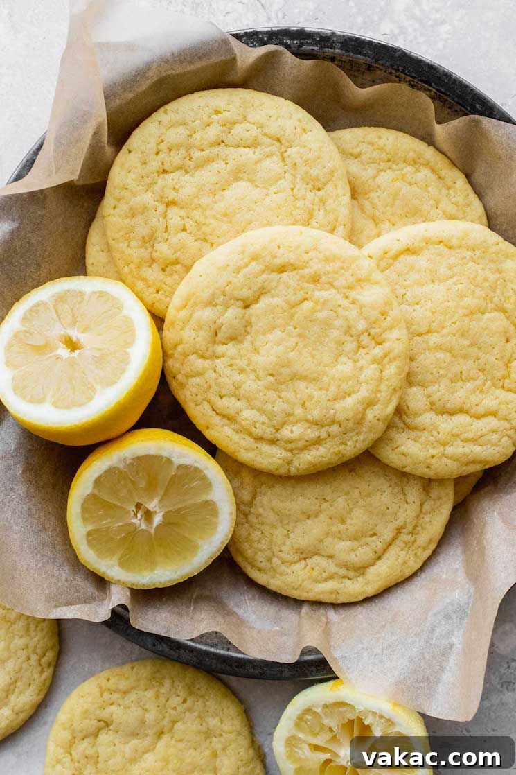 Tangy Lemon Delights 2 A round pan filled with freshly baked, soft lemon cookies, with a vibrant lemon cut in half resting beside them, highlighting the key ingredient.