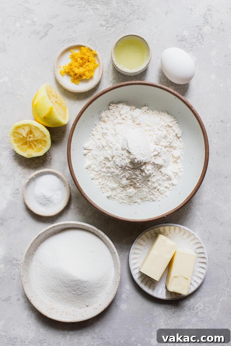 Tangy Lemon Delights 3 A collection of fresh ingredients for lemon cookies laid out on a clean gray surface, including lemons, flour, butter, sugar, and eggs.