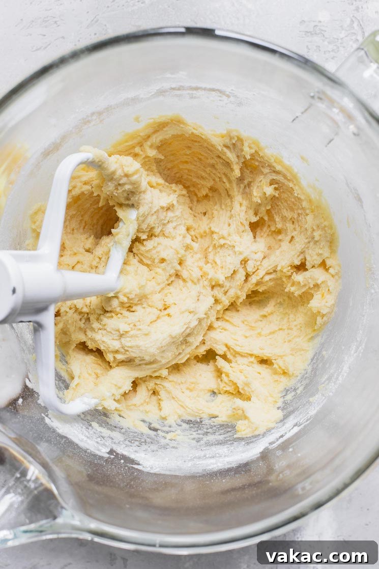 A glass mixing bowl containing creamy cookie batter, with the beater of a stand mixer still resting in it, ready for the next step.