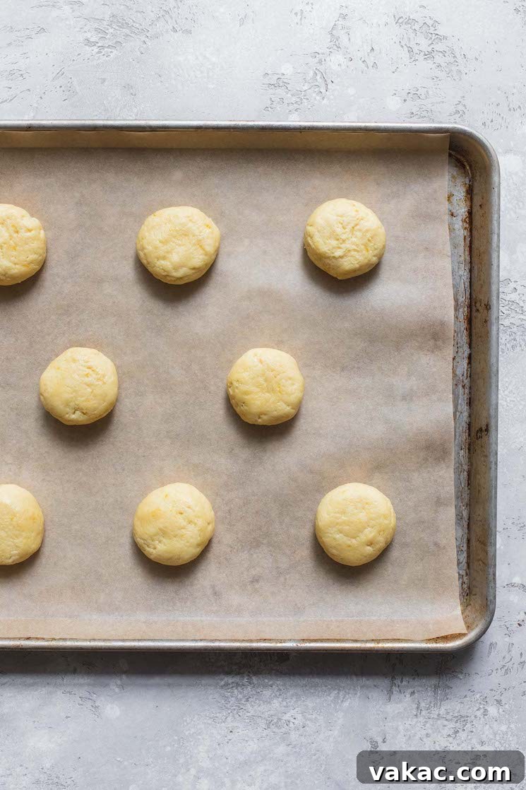 A baking sheet lined with parchment paper, neatly arranged with scoops of lemon cookie dough, perfectly spaced and ready for baking.