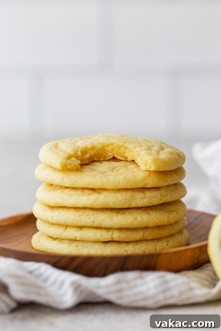 Tangy Lemon Delights 6 A delightful stack of perfectly baked lemon cookies rests on a rustic wooden plate, with the top cookie showing a mouth-watering bite taken out of it.