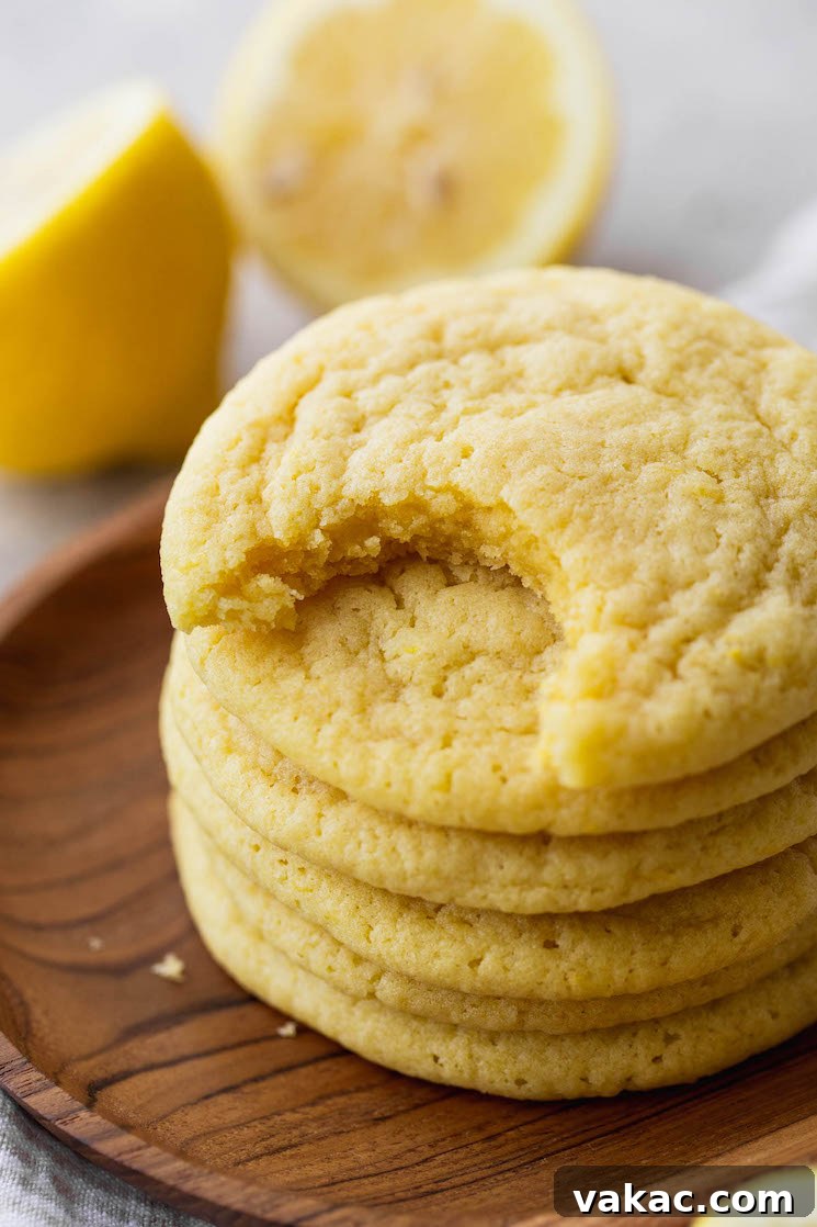 Tangy Lemon Delights 7 A close-up photograph of a stack of golden lemon cookies on a wooden surface, clearly showing a bite taken from the top cookie, revealing its soft, chewy interior.
