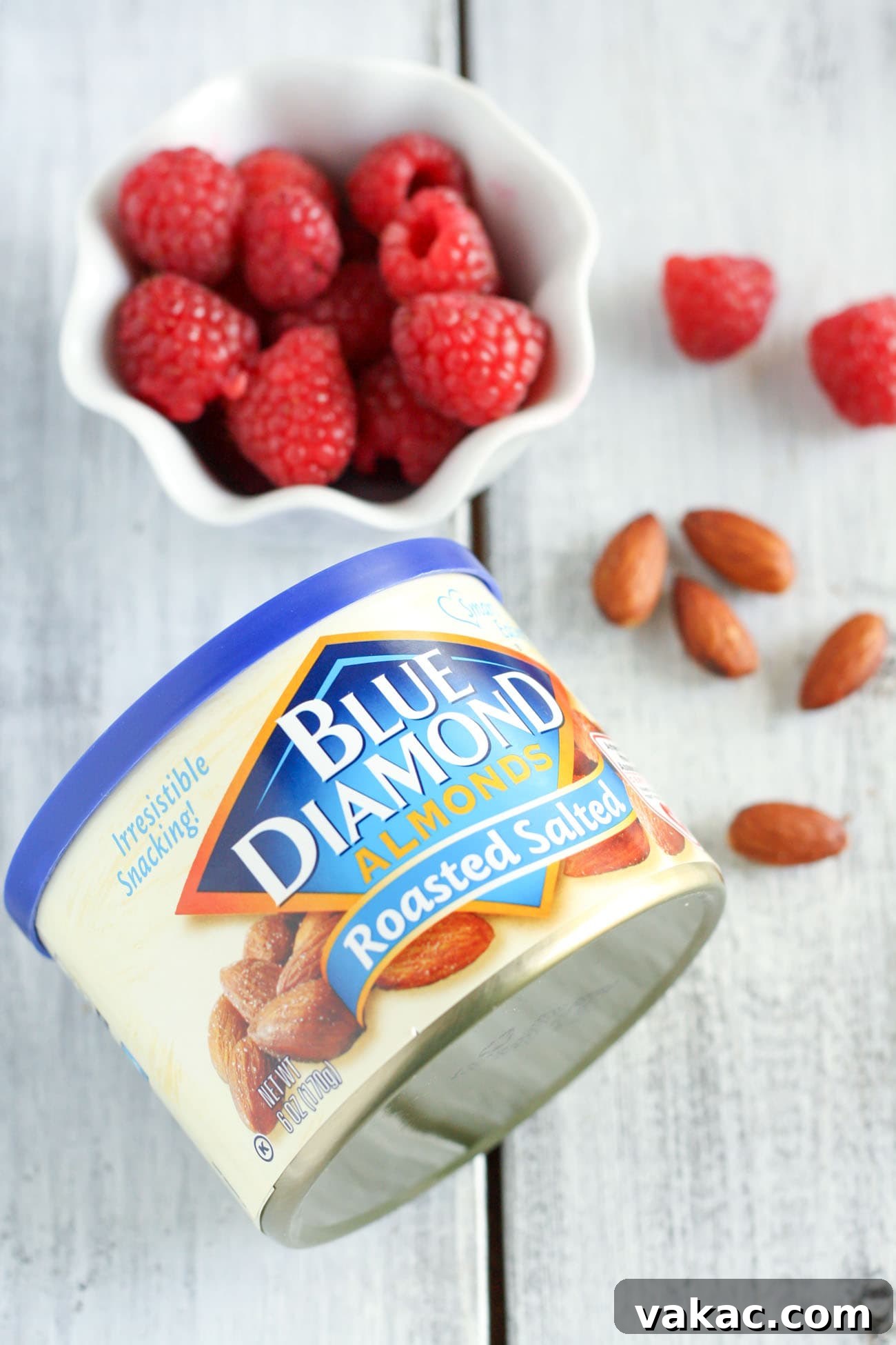 Blissful Raspberry Almond Cake 3 A clear glass dish overflowing with vibrant fresh raspberries sits next to a container of Blue Diamond Roasted Salted Almonds, highlighting the key ingredients of this delicious cake.