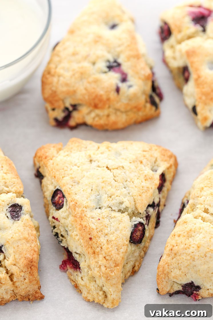Bright Lemon Blueberry Scones 4 A captivating close-up of freshly baked lemon blueberry scones arranged on parchment paper, awaiting their final touch. In the background, a small glass bowl holds the luscious lemon glaze, ready to be drizzled over these delectable pastries.