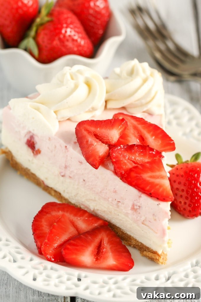 Velvet Strawberry Vanilla Bean Cheesecake 3 A pristine slice of no-bake strawberry cheesecake elegantly presented on a white plate, garnished with vibrant berry slices. In the background, a bowl brimming with fresh berries and a fork patiently await, hinting at more delicious moments.