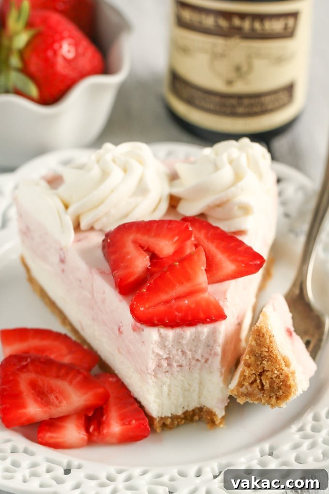 Velvet Strawberry Vanilla Bean Cheesecake 5 A delectable slice of no-bake strawberry cheesecake artfully presented on a white dessert plate, adorned with fresh berry slices and accompanied by a fork. In the background, a bottle of vanilla extract stands, hinting at the key flavor enhancer in this sweet creation.