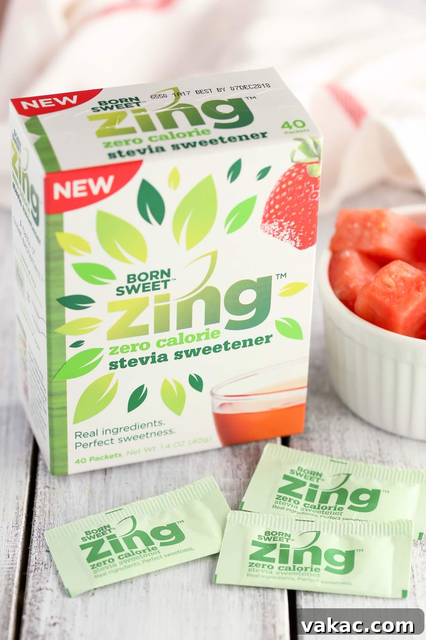 Zesty Watermelon Freeze 4 A person pouring a vibrant watermelon lime slushie from a blender into a tall glass, with frozen watermelon cubes, lime, and Zing Stevia packets on the counter.