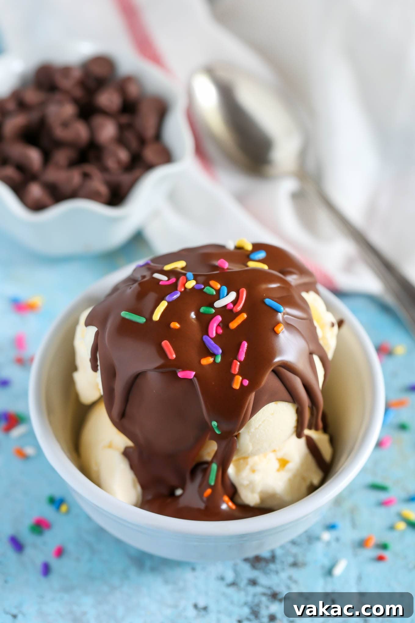 DIY Chocolate Crunch Topping 4 A small dish of vanilla ice cream topped with magic shell and sprinkles. A dish of chocolate chips and a spoon rest in the background.