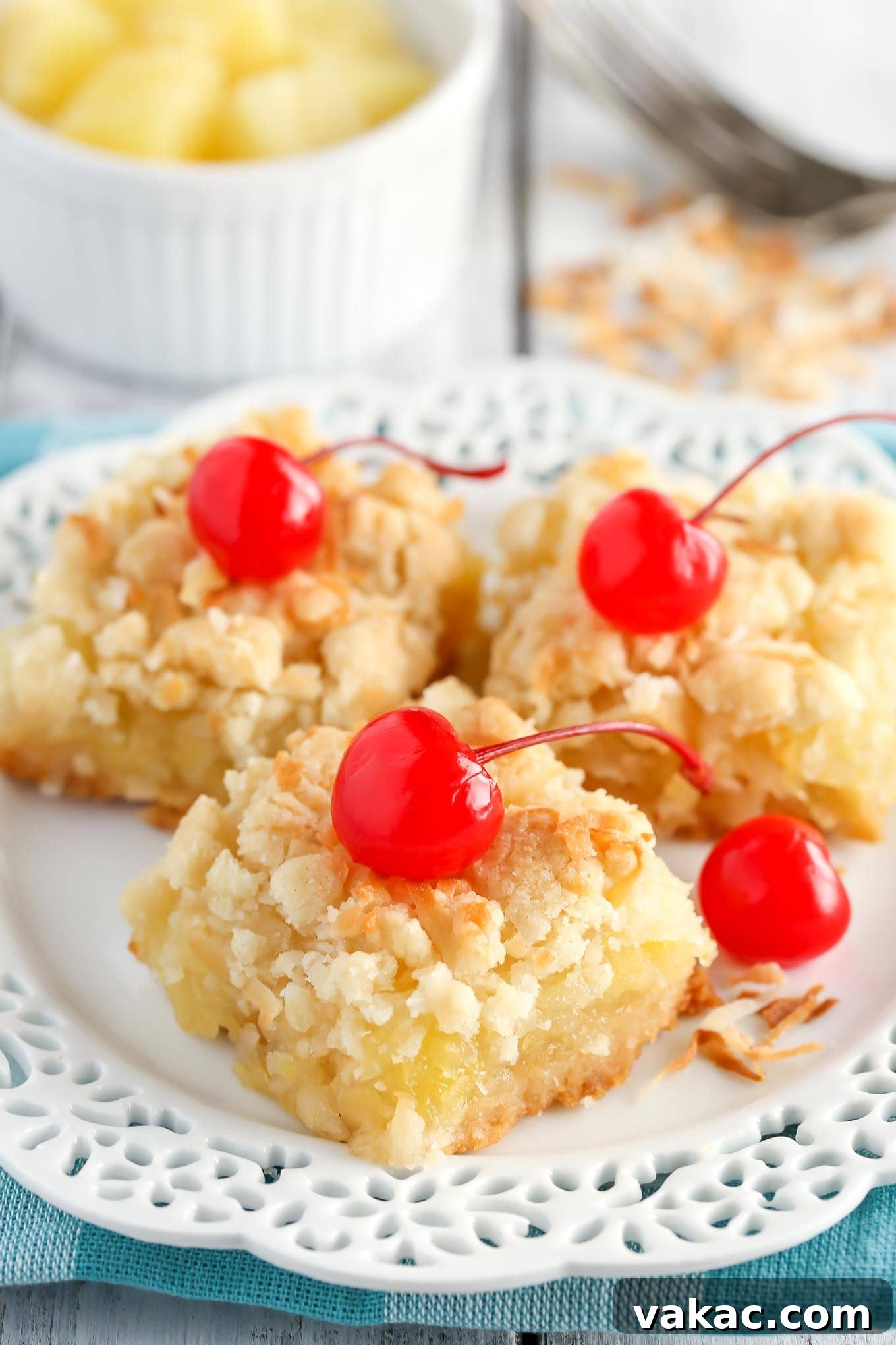 Golden Pineapple Squares 2 Three pineapple bars garnished with maraschino cherries on a white dessert plate. A small bowl of pineapple rests in the background.