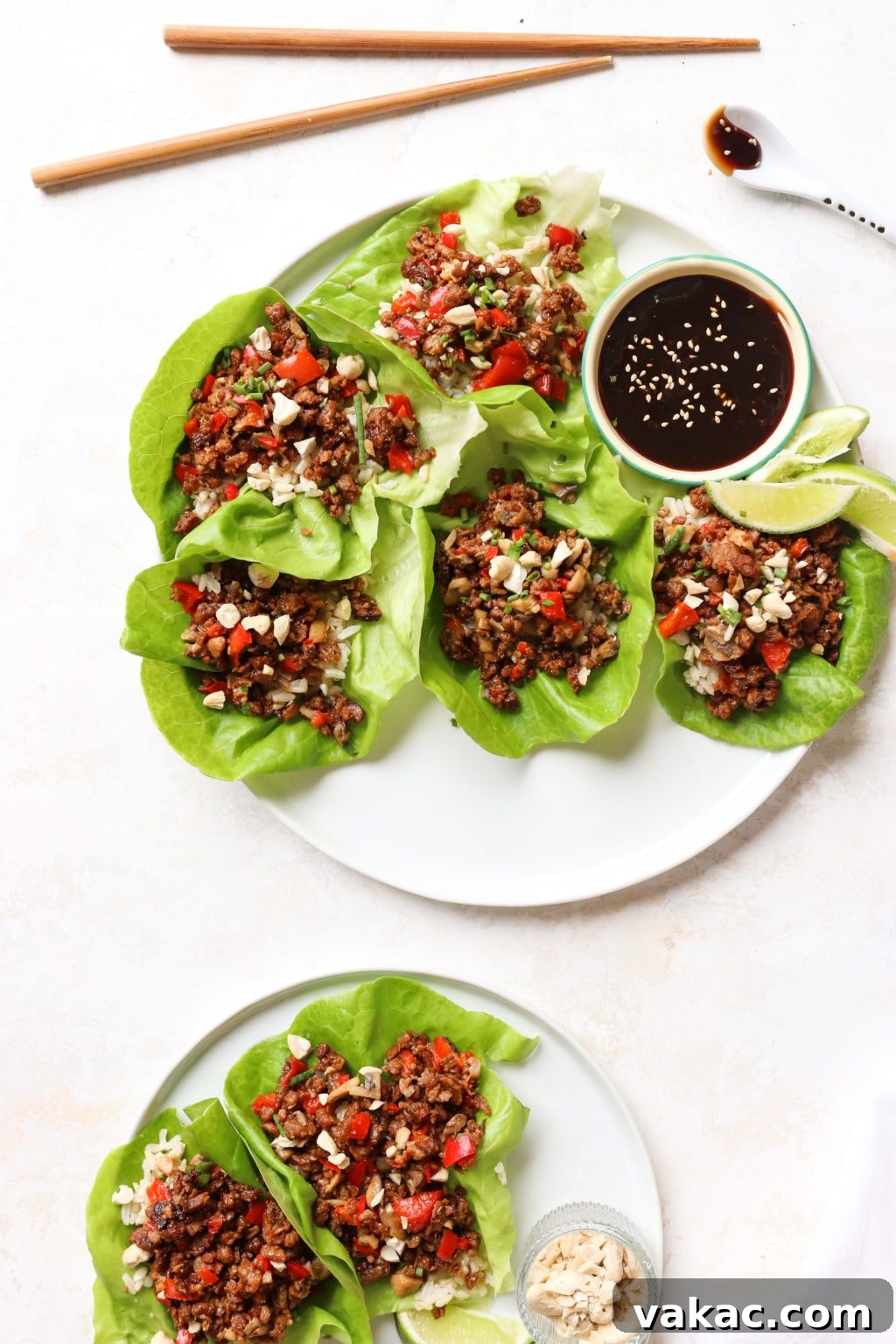 Healthy Ground Beef Lettuce Wraps for Effortless Meal Prep 2 A beautifully arranged white plate showcasing five open-face lettuce wraps alongside a small bowl of savory hoisin sauce. Chopsticks and a white spoon, glistening with hoisin, are positioned elegantly at the top of the frame.