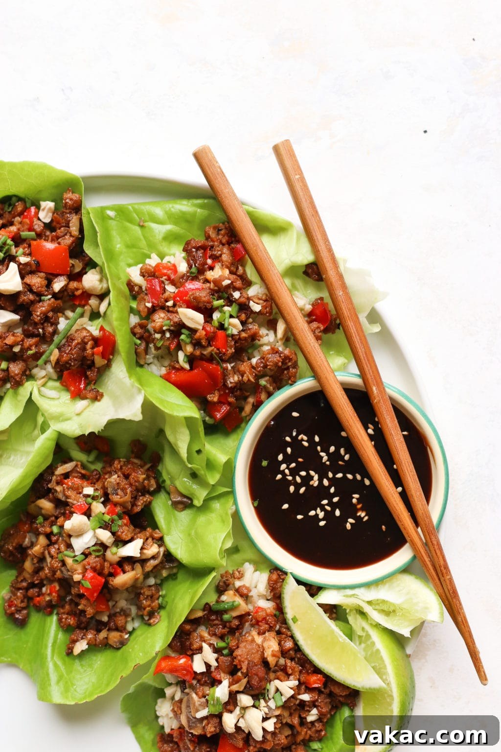 Healthy Ground Beef Lettuce Wraps for Effortless Meal Prep 3 A close-up shot of a white plate, focused on three open-face lettuce wraps accompanied by a small bowl of hoisin sauce. Two chopsticks rest gracefully on top of the hoisin bowl.