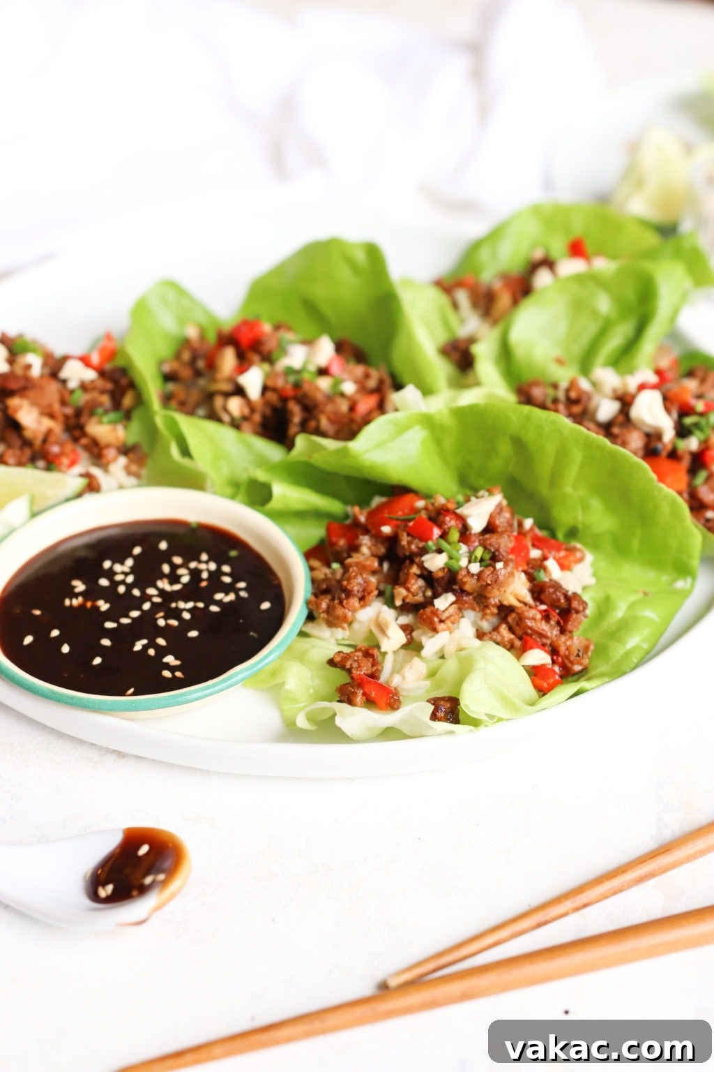 Healthy Ground Beef Lettuce Wraps for Effortless Meal Prep 4 A close-up photograph of a white plate featuring three open-face lettuce wraps. A small bowl of hoisin sauce is placed adjacent to the wraps, ready for dipping.