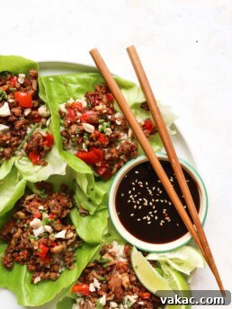 A close-up shot of a white plate, focused on three open-face lettuce wraps accompanied by a small bowl of hoisin sauce. Two chopsticks rest gracefully on top of the hoisin bowl.