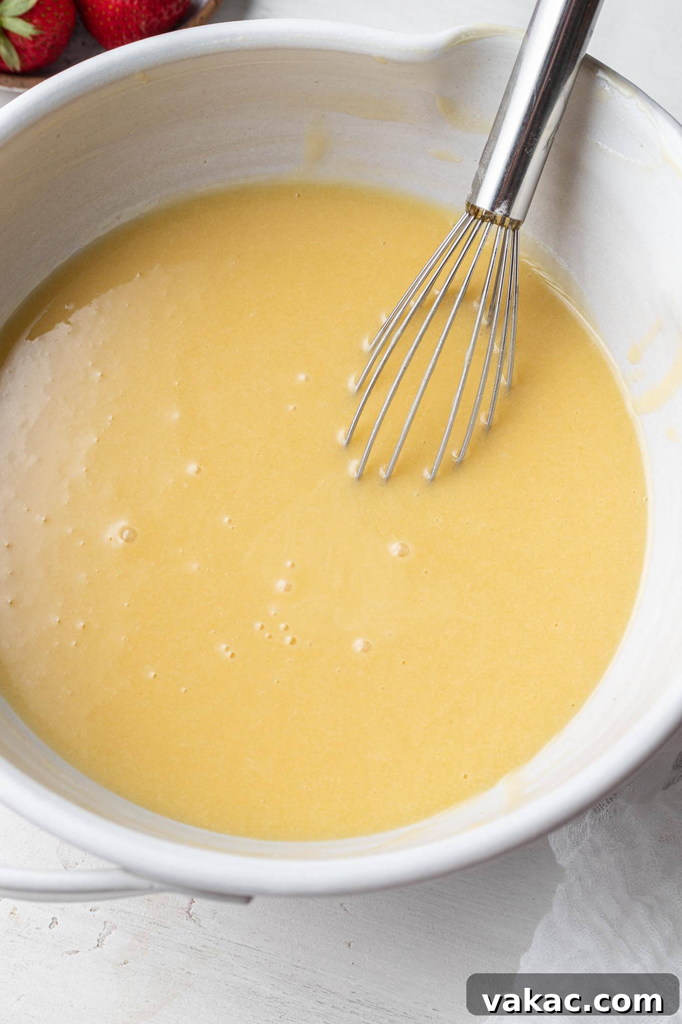 Egg yolk mixture in a mixing bowl with a whisk, showcasing a smooth, creamy texture.