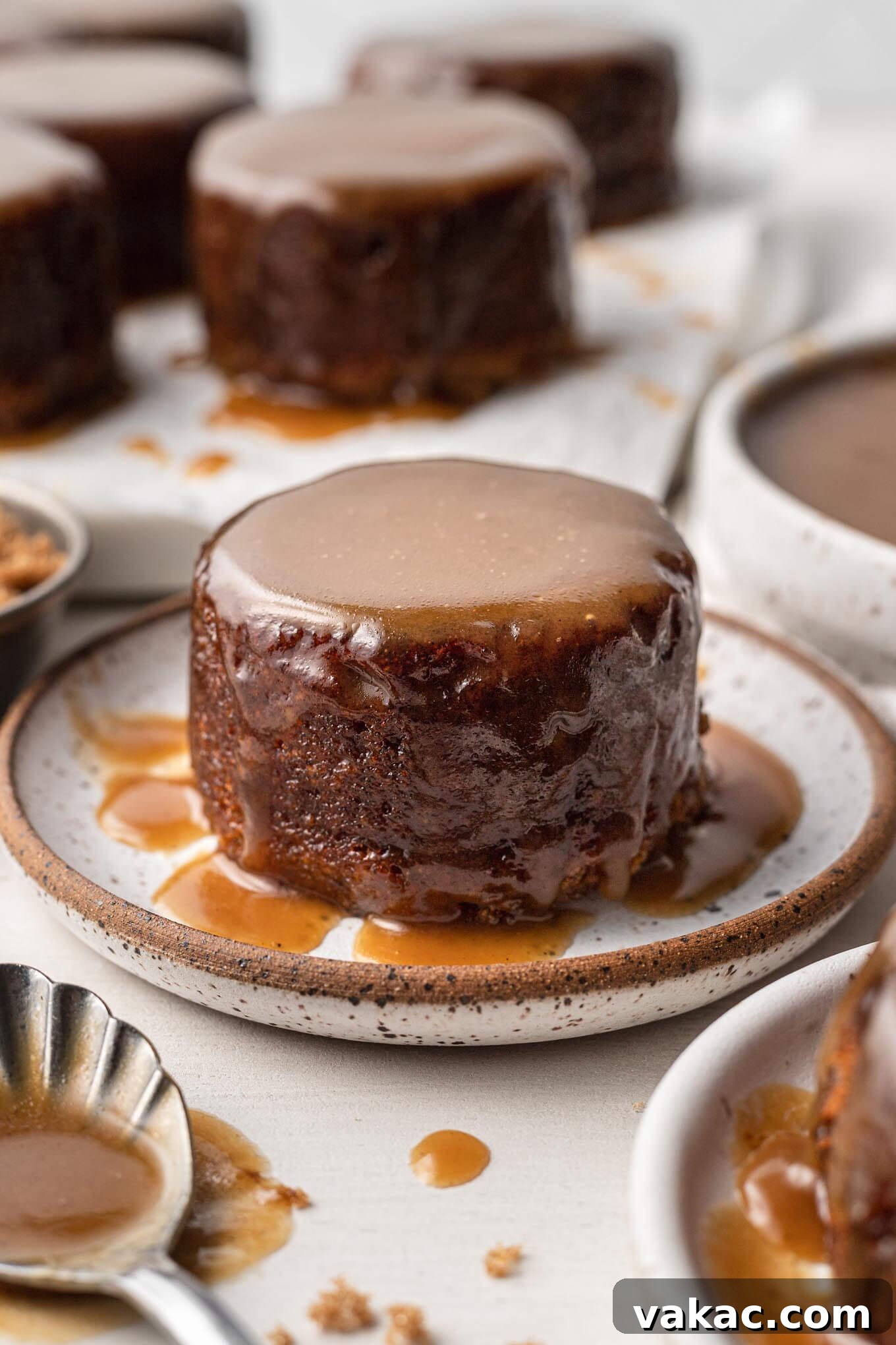 Caramel Date Delight 2 A sticky toffee pudding on a speckled plate. More rest in the background.