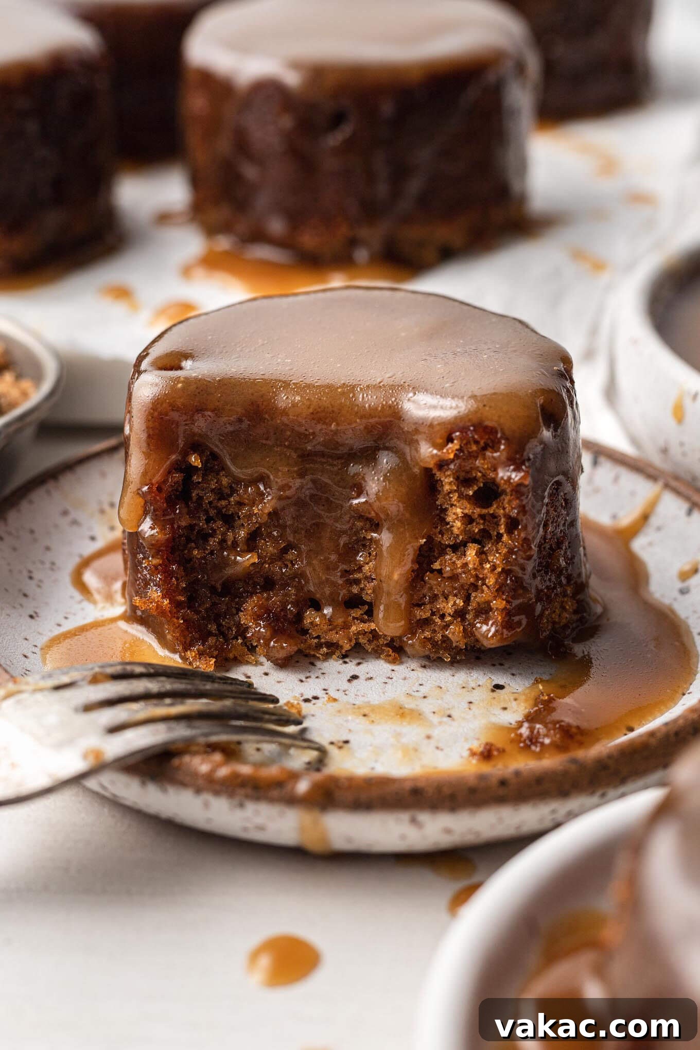 Caramel Date Delight 9 A piece of sticky toffee pudding on a white speckled plate. A bite has been taken out and a fork rests on the plate.