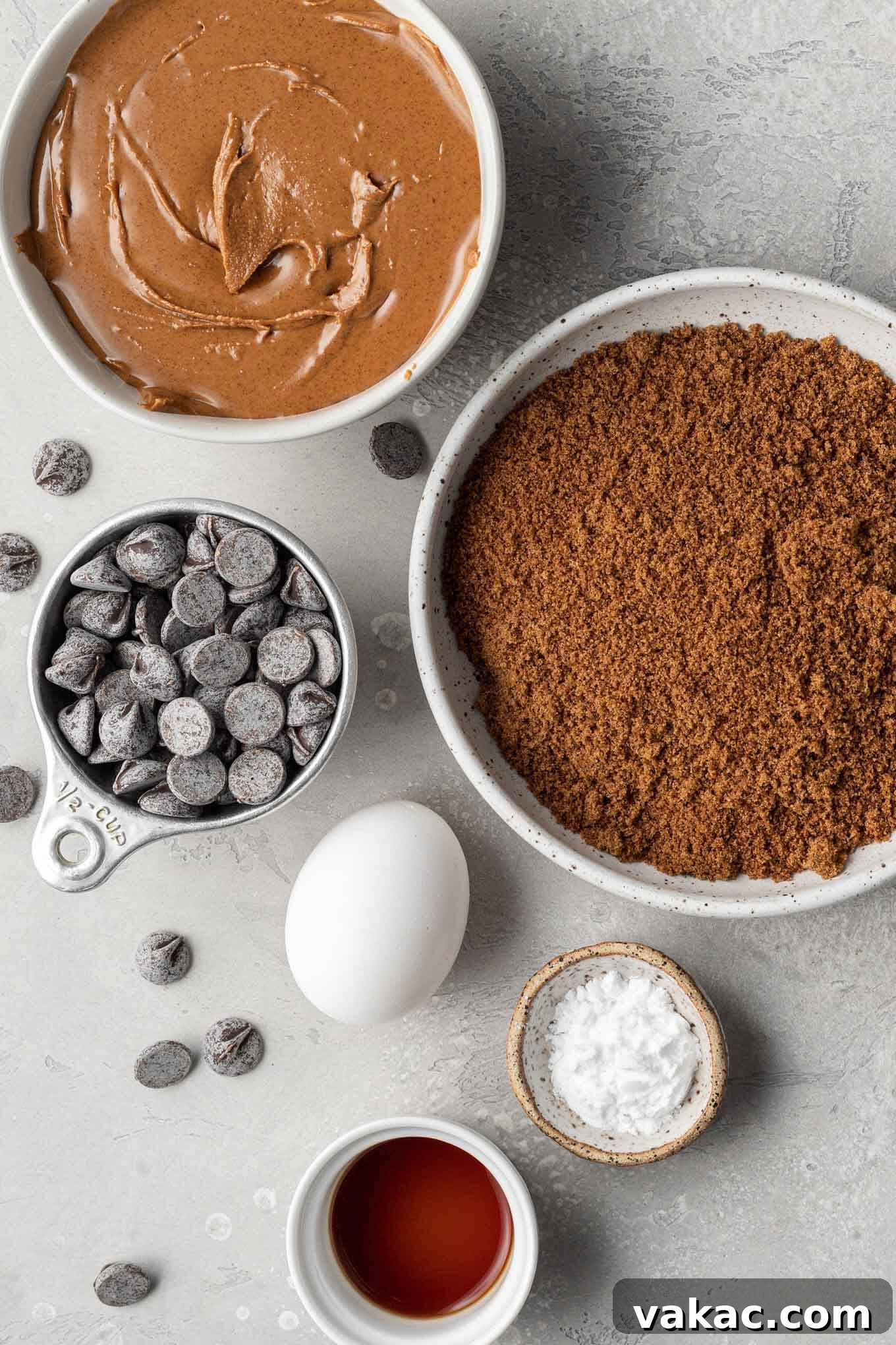 Irresistible Flourless Almond Butter Cookies 3 An overhead view displaying all the essential ingredients laid out neatly, ready to make almond butter chocolate chip cookies: a jar of almond butter, coconut sugar, an egg, vanilla extract, baking soda, and a bowl of chocolate chips.
