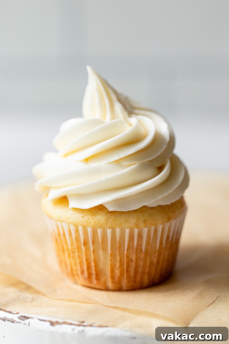 A single cupcake generously topped with perfectly piped buttercream frosting, resting on a rustic wooden surface with brown parchment paper.