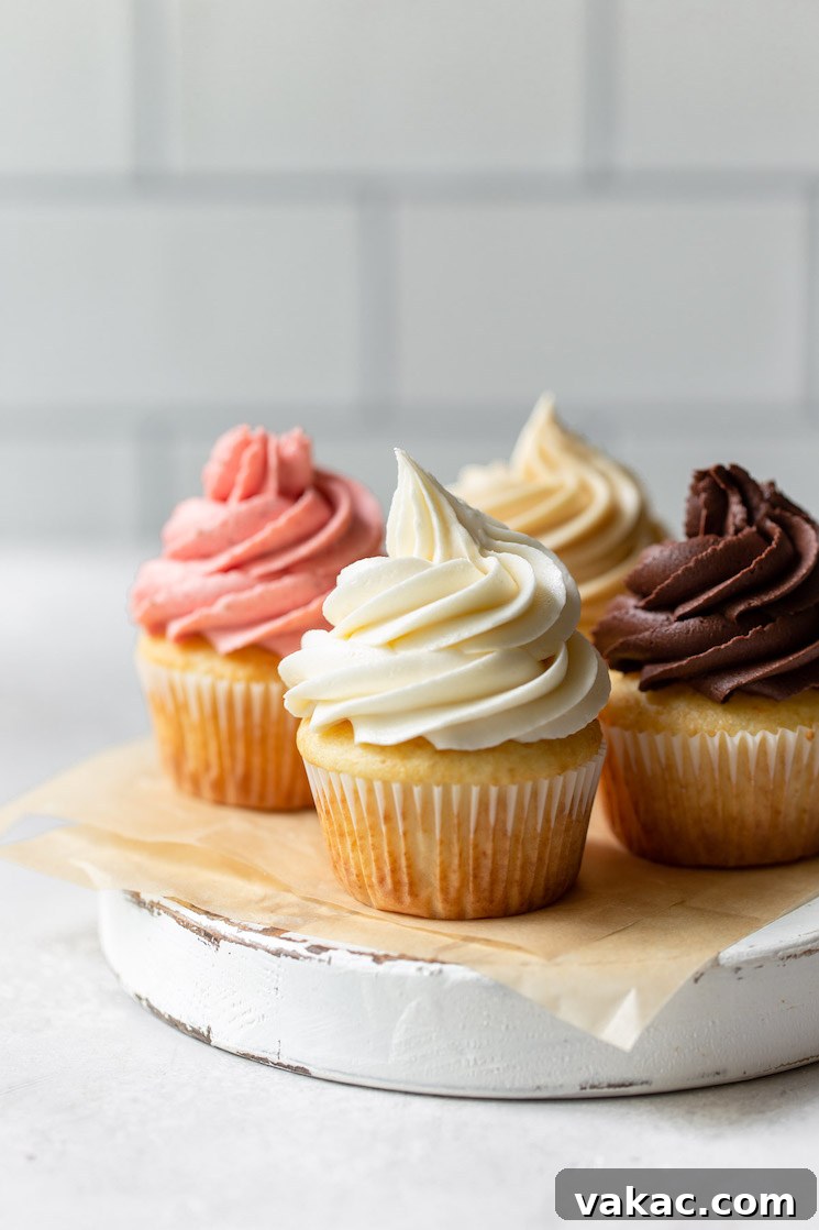 Four beautifully decorated cupcakes, each topped with a different flavor of vibrant buttercream frosting, arranged artfully on a rustic round wooden serving board.