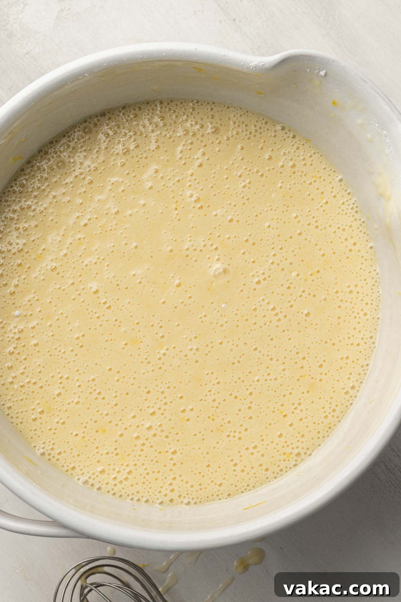 Smooth and perfectly mixed lemon olive oil cake batter, with a faint yellow hue, resting in a white ceramic mixing bowl, ready for baking.