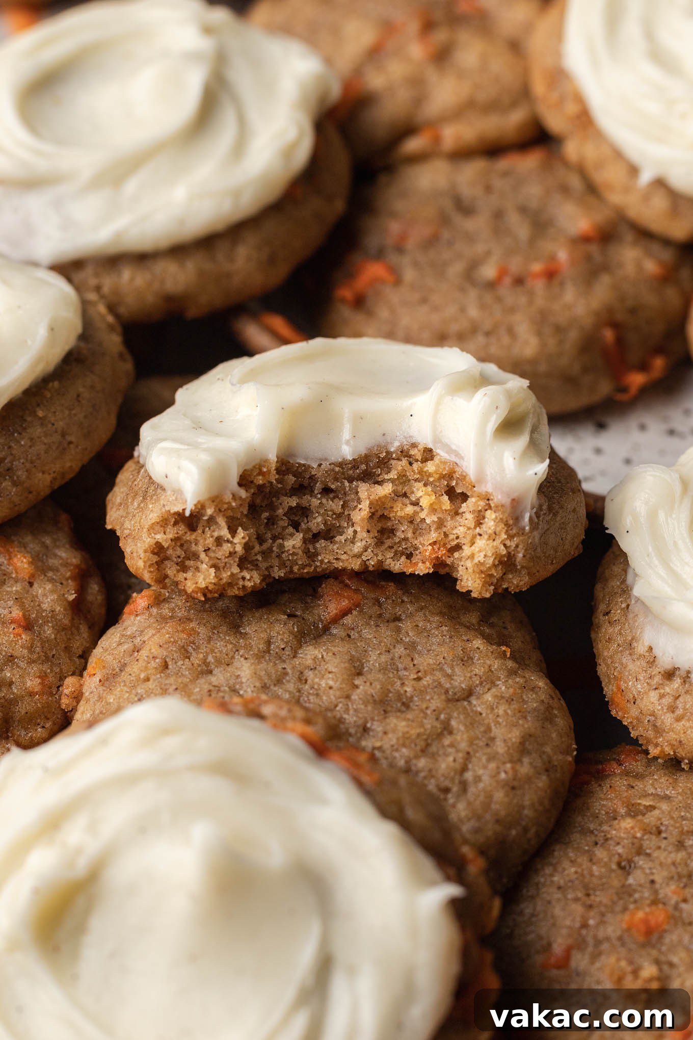 A close-up view of a frosted carrot cake cookie with a bite missing. 