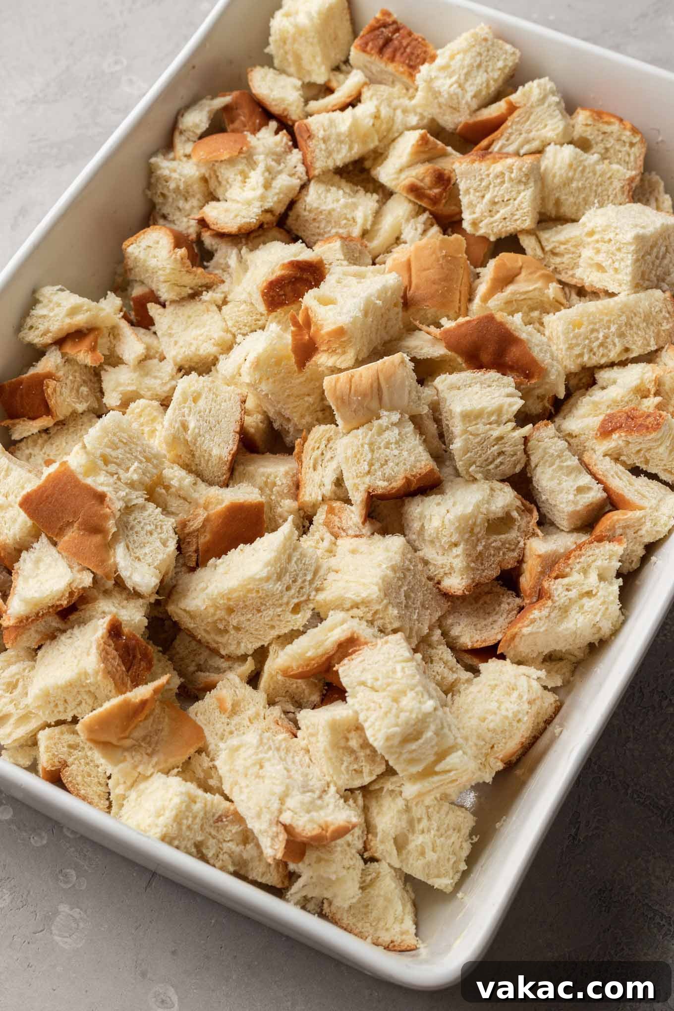 Overnight French Toast Bake 4 Cubes of golden challah bread are neatly arranged in a white ceramic casserole dish, ready for the custard mixture.