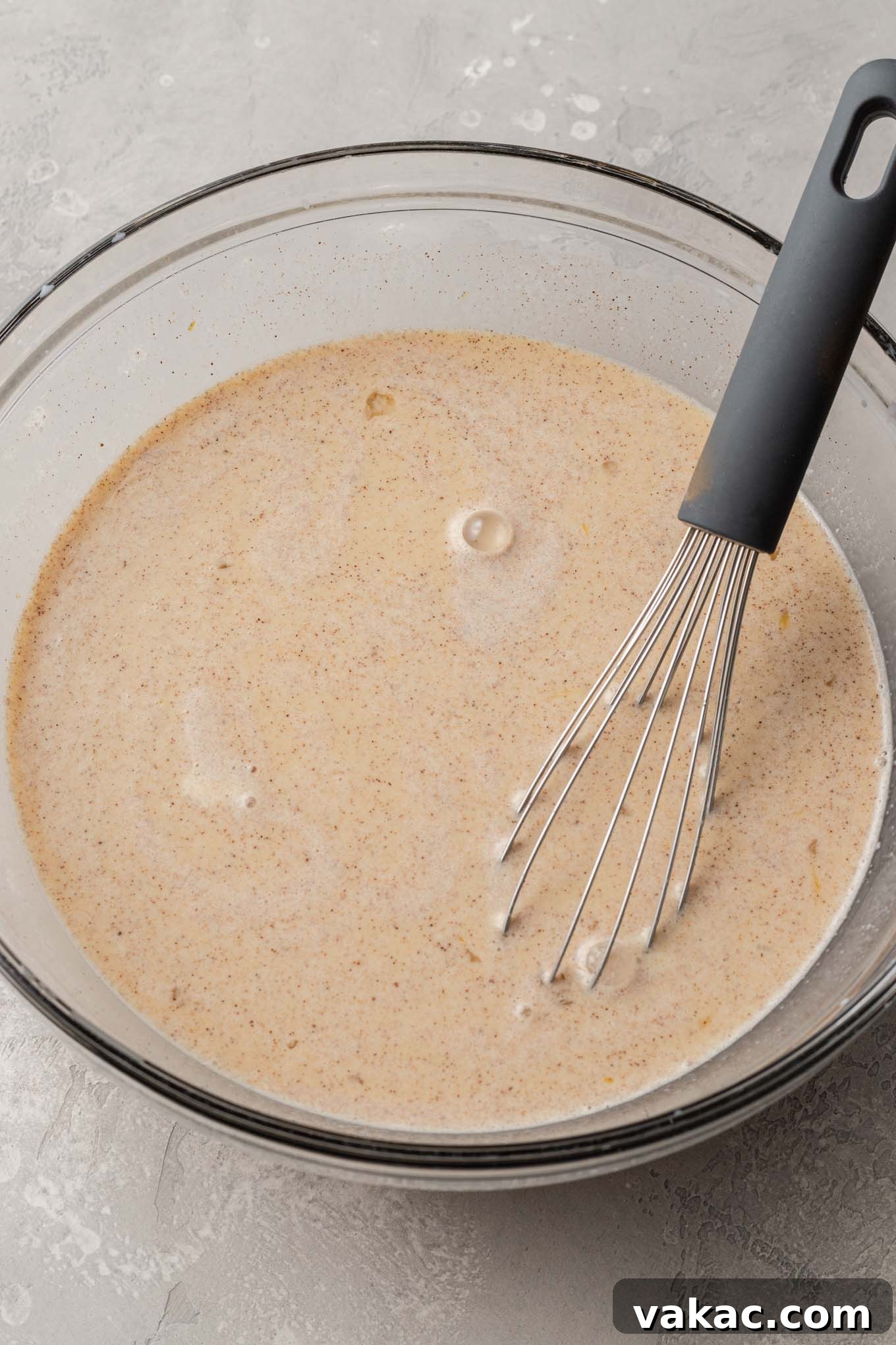 Overnight French Toast Bake 5 A clear glass mixing bowl holds a perfectly whisked, creamy spiced custard mixture, ready to be poured over the bread.