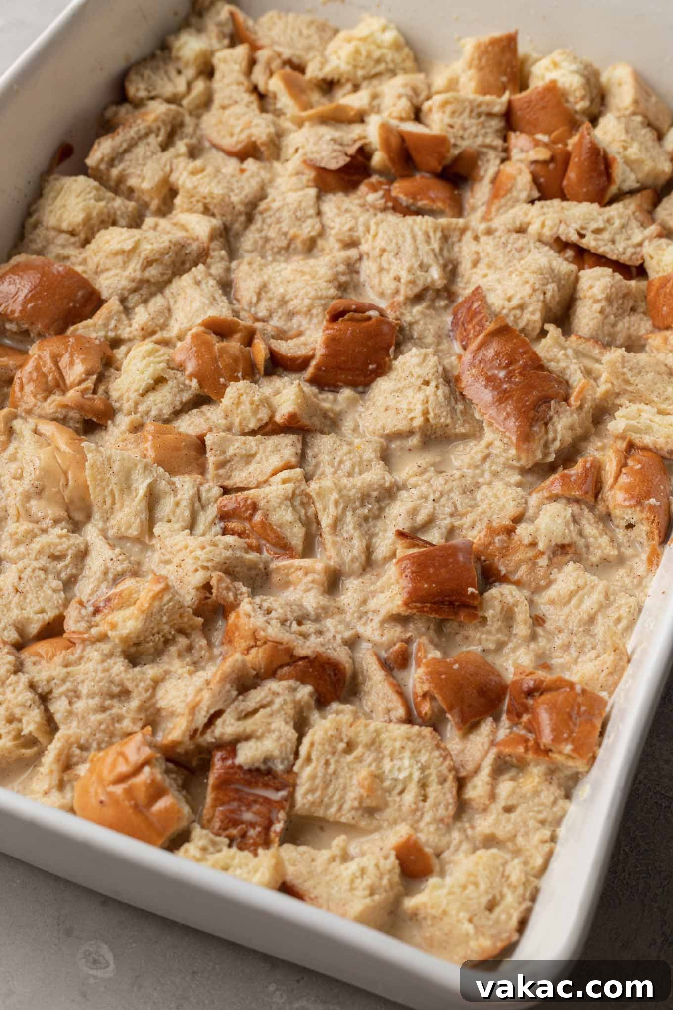 Overnight French Toast Bake 6 An unbaked challah French toast casserole in a white baking dish, with the rich custard fully poured over and soaking into the cubed bread.
