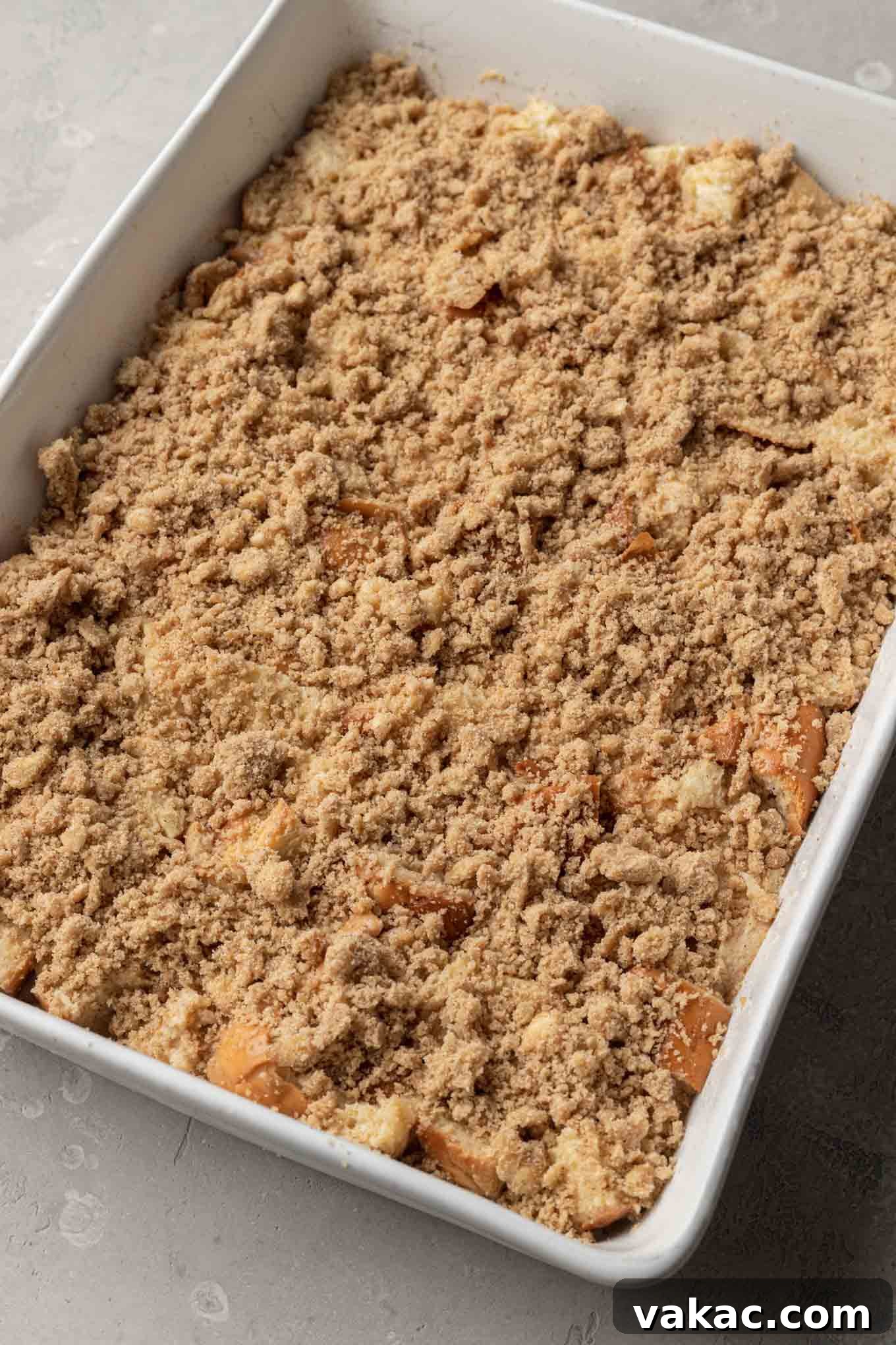 Overnight French Toast Bake 7 The unbaked challah French toast casserole in a white baking dish, now beautifully topped with a generous layer of golden, crumbly streusel, ready for baking.
