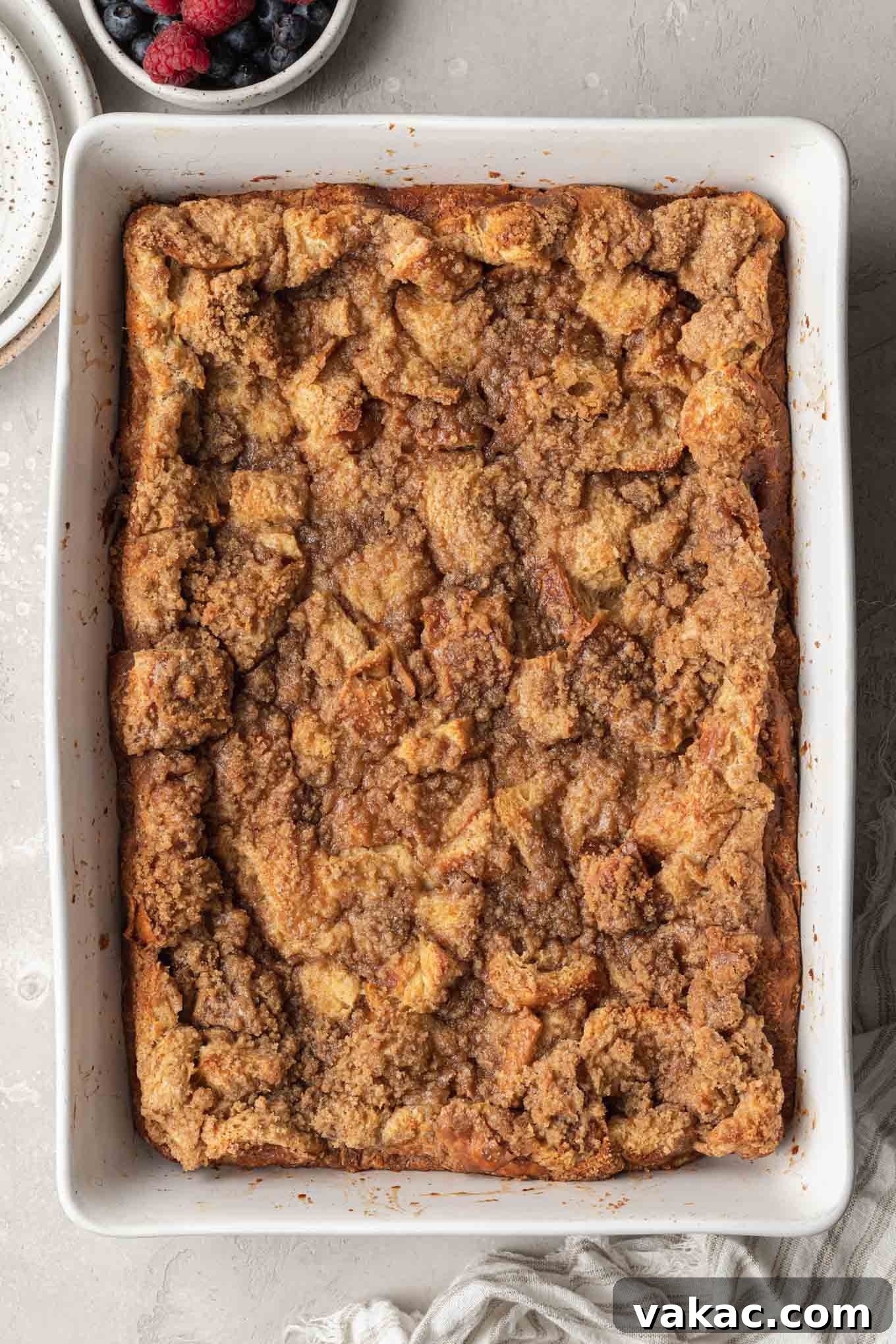 Overnight French Toast Bake 8 An inviting overhead view of a freshly baked French toast breakfast casserole in a white baking dish, generously topped with a golden-brown crumbly streusel.