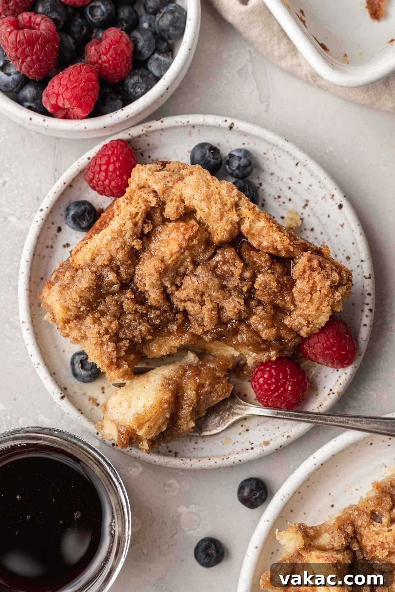 Overnight French Toast Bake 9 An overhead shot of a serving of baked French toast casserole on a plate, accompanied by a small bowl of fresh blueberries and raspberries, highlighting the golden crumb topping.