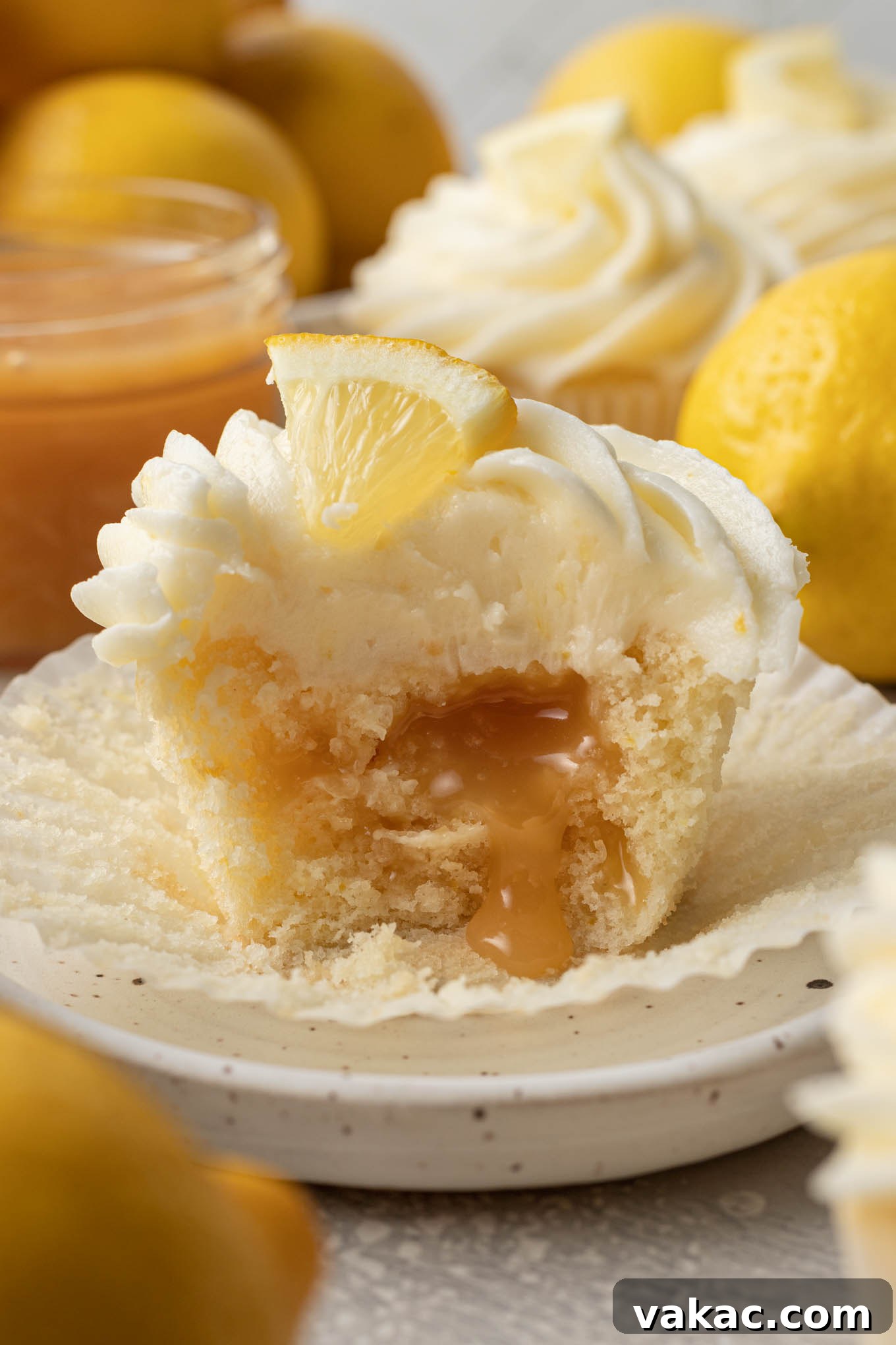 Sunshine Lemon Bliss Cupcakes 9 A tantalizing close-up of a lemon curd filled cupcake with a bite taken out, showcasing the gooey, vibrant lemon curd oozing out from the center, on a light background.