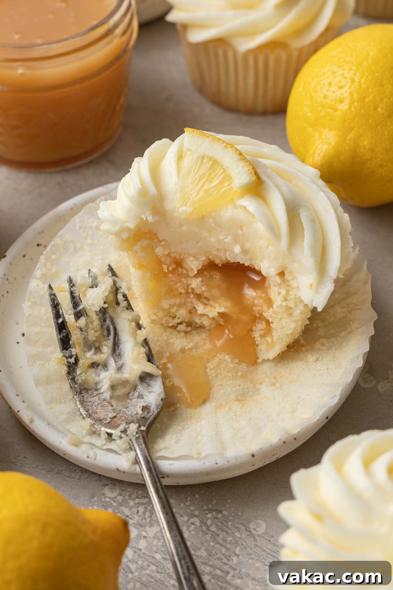 Sunshine Lemon Bliss Cupcakes 10 A single, beautifully frosted lemon curd cupcake resting on a simple white dessert plate, with a small piece taken out to reveal the tangy lemon curd inside. A perfect close-up of this delightful treat.