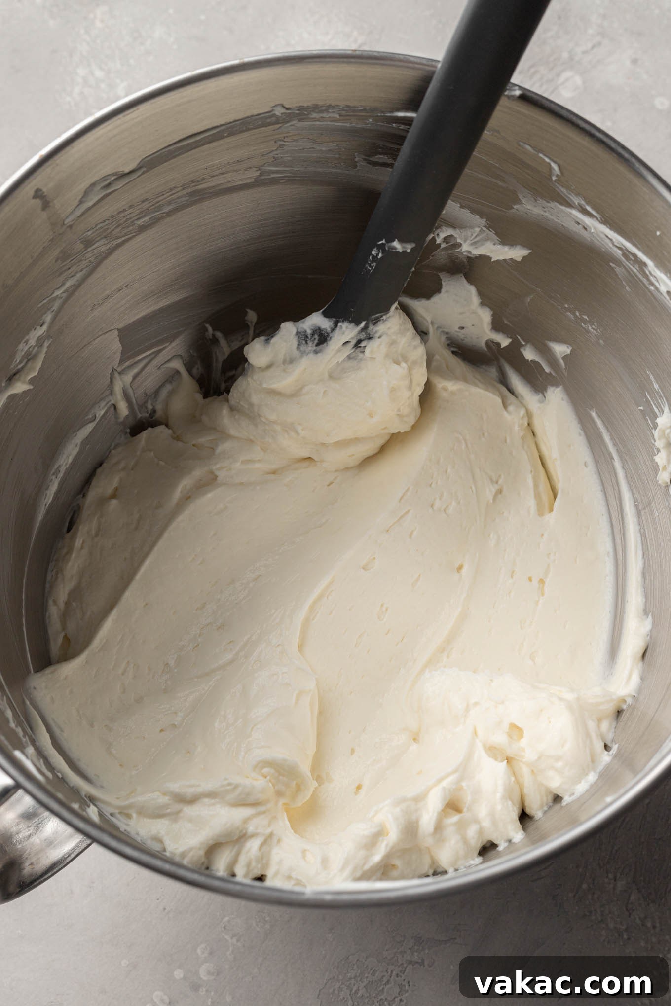 Effortless Mini Cheesecake Delights 6 An overhead view of the smooth cheesecake mixture in a mixing bowl, with a rubber spatula used to scrape down the sides.