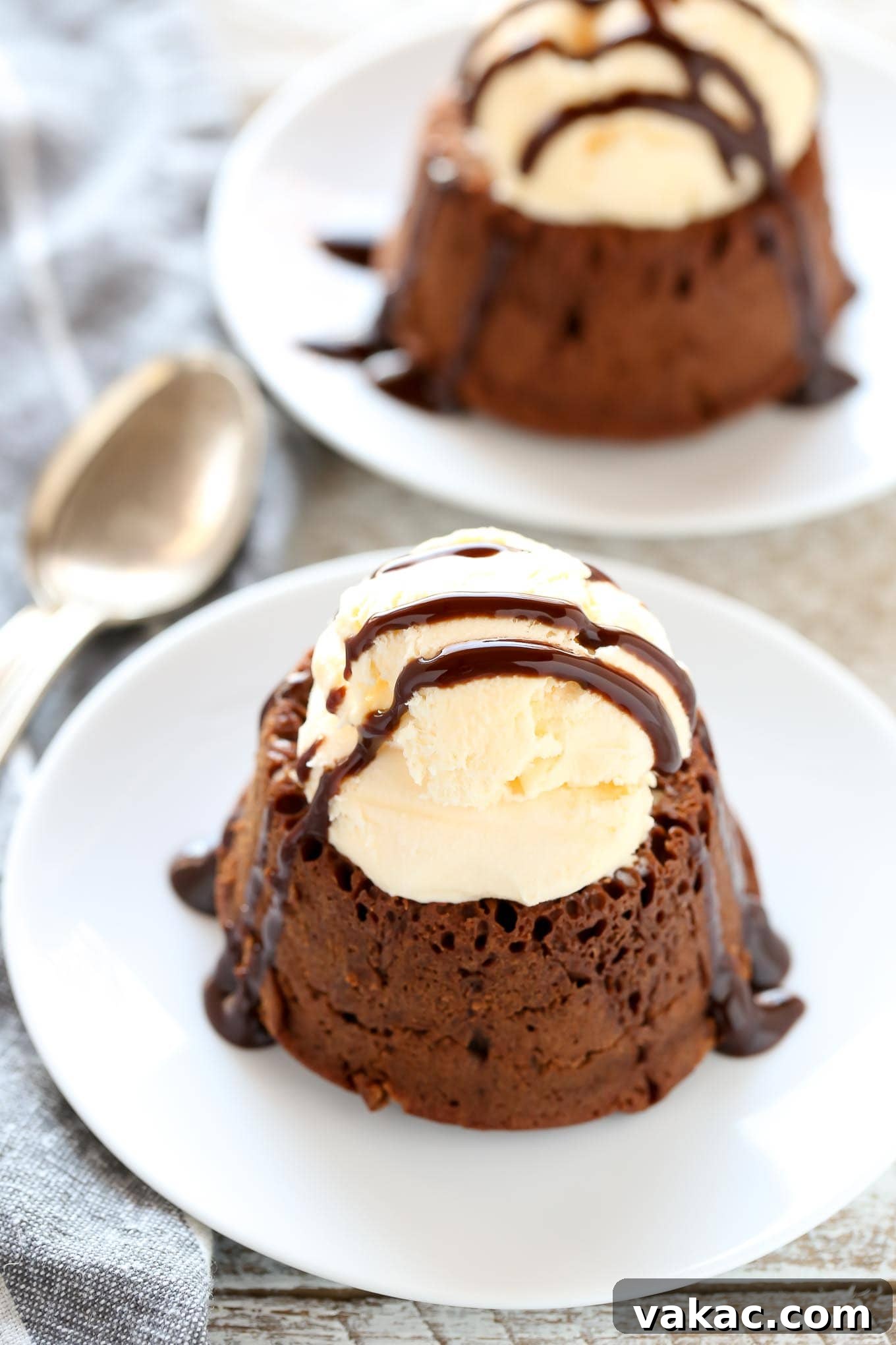 Decadent Molten Chocolate Lava Cake Perfection 2 Two chocolate lava cakes topped with a scoop of ice cream and a drizzle of chocolate sauce. Both are on white dessert plates.