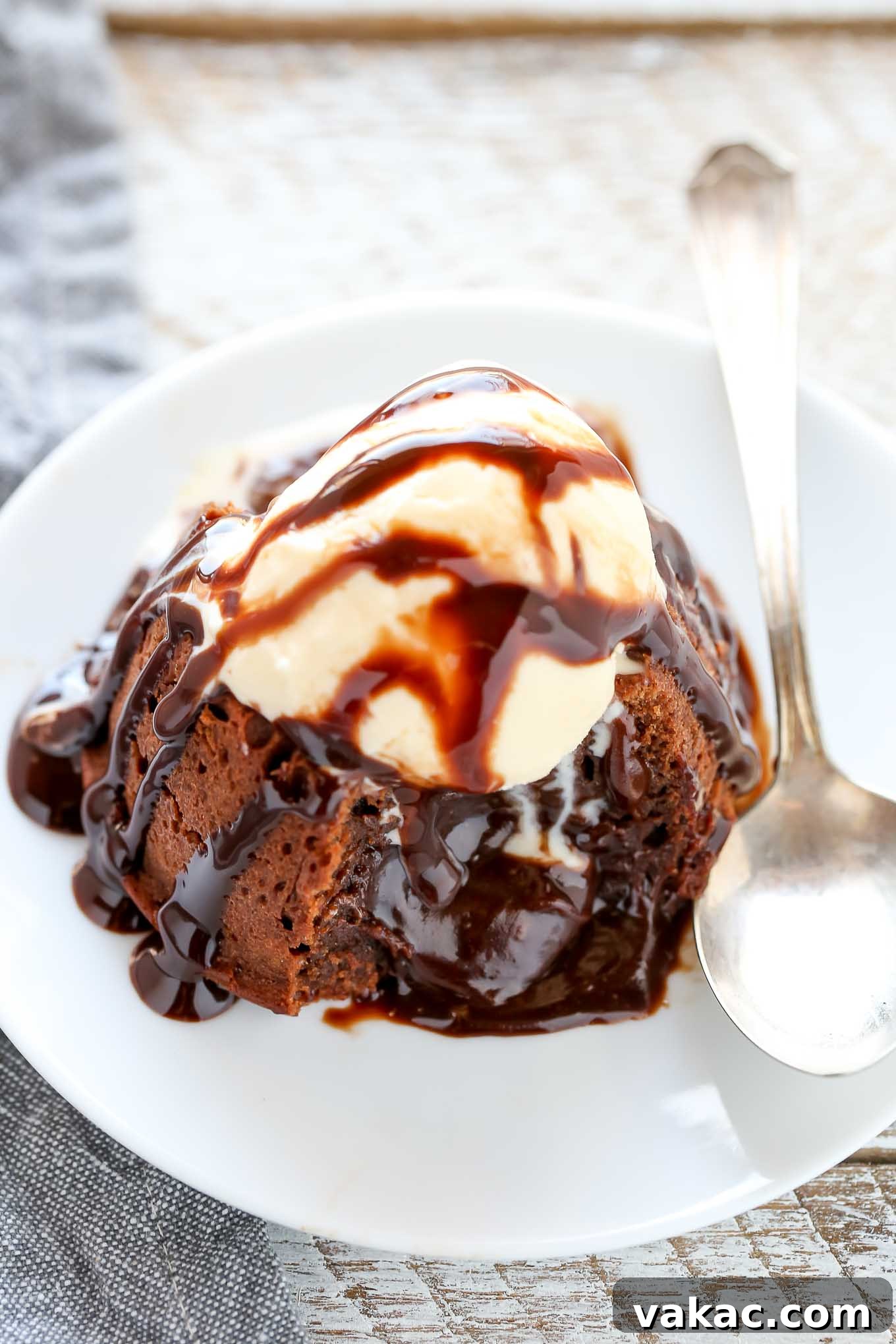 Decadent Molten Chocolate Lava Cake Perfection 7 A molten lava cake topped with ice cream and chocolate sauce on a white plate. The cake has been cut into and the filling is oozing out.