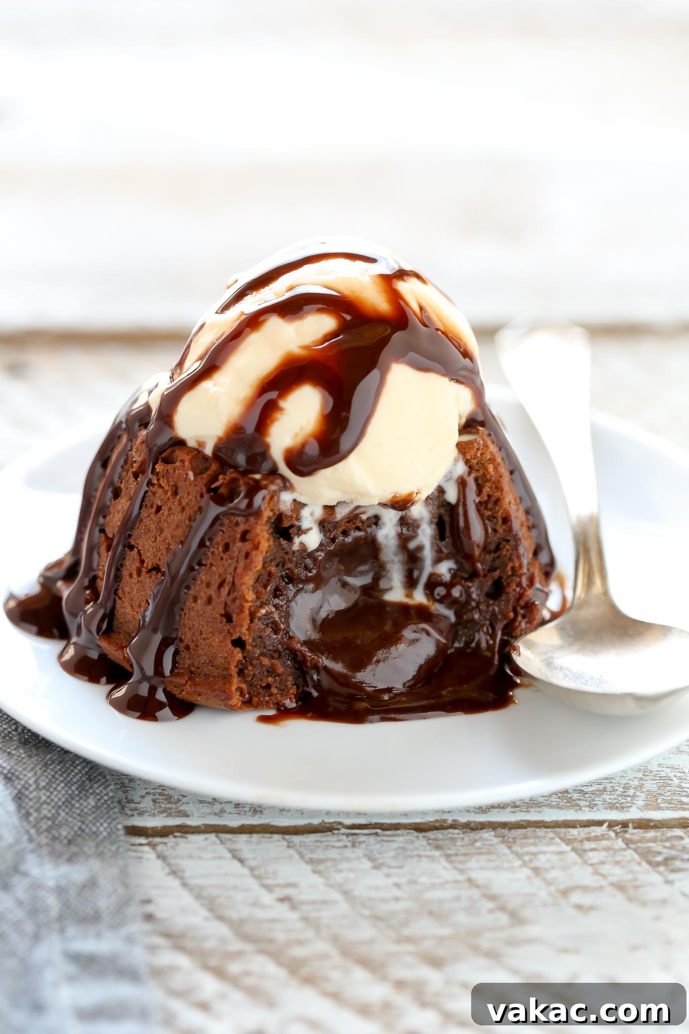 Decadent Molten Chocolate Lava Cake Perfection 6 A molten chocolate cake topped with ice cream and chocolate sauce on a white plate. The cake has been cut into and the filling is oozing out.