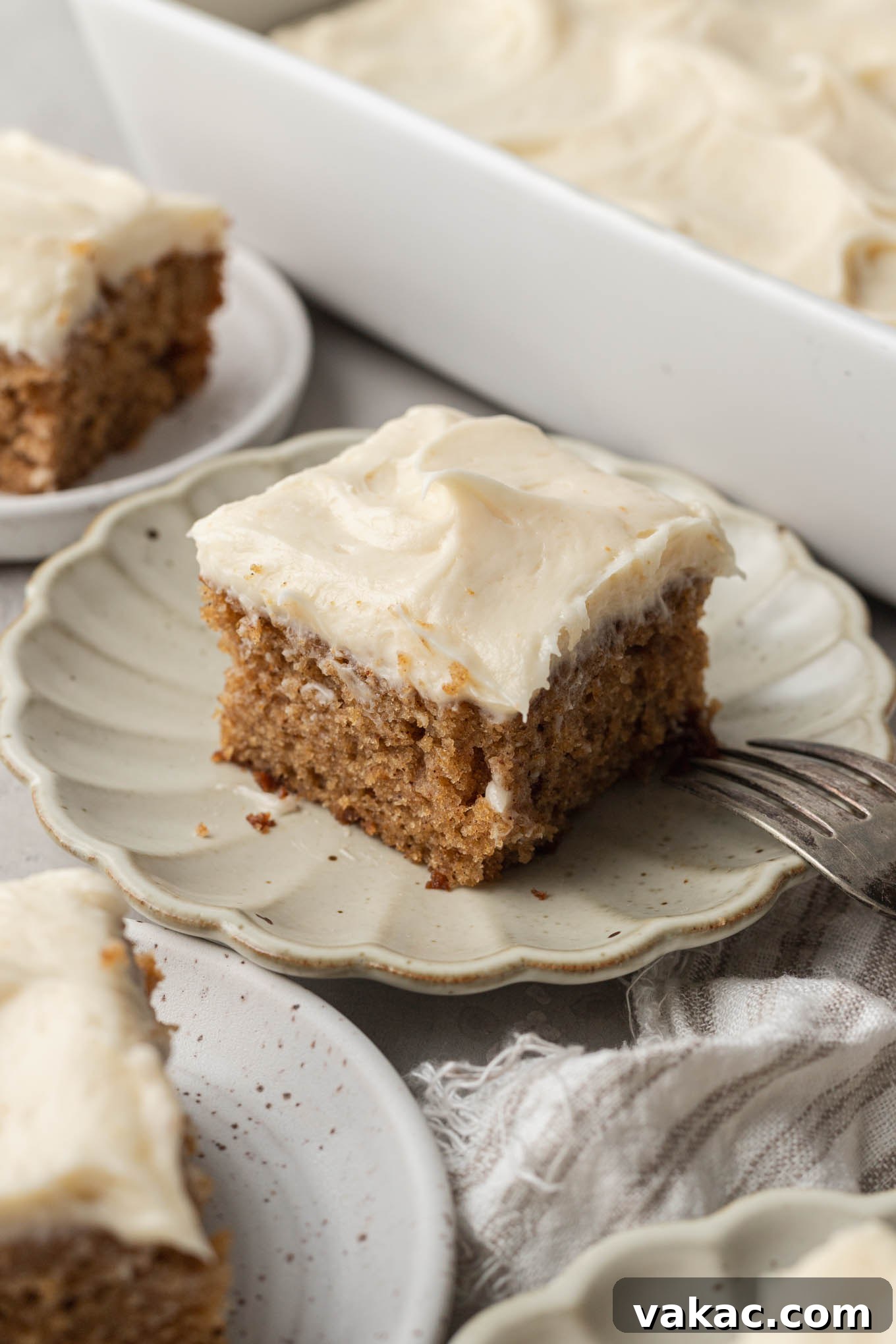 A perfectly sliced piece of moist applesauce cake topped with creamy brown butter frosting, presented on an elegant scalloped cream dessert plate, ready to be enjoyed.