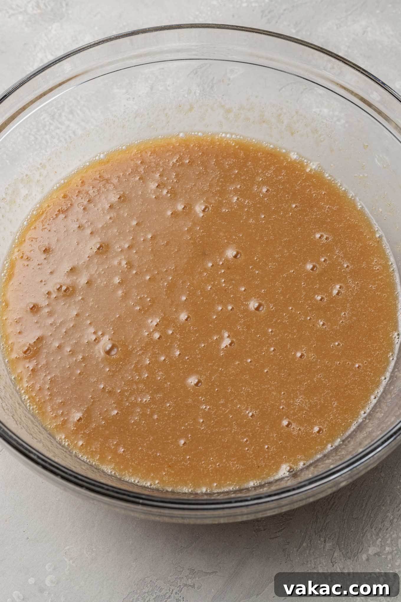 A glass mixing bowl holds the carefully combined wet ingredients for a delicious applesauce cake, captured from an appealing overhead perspective.
