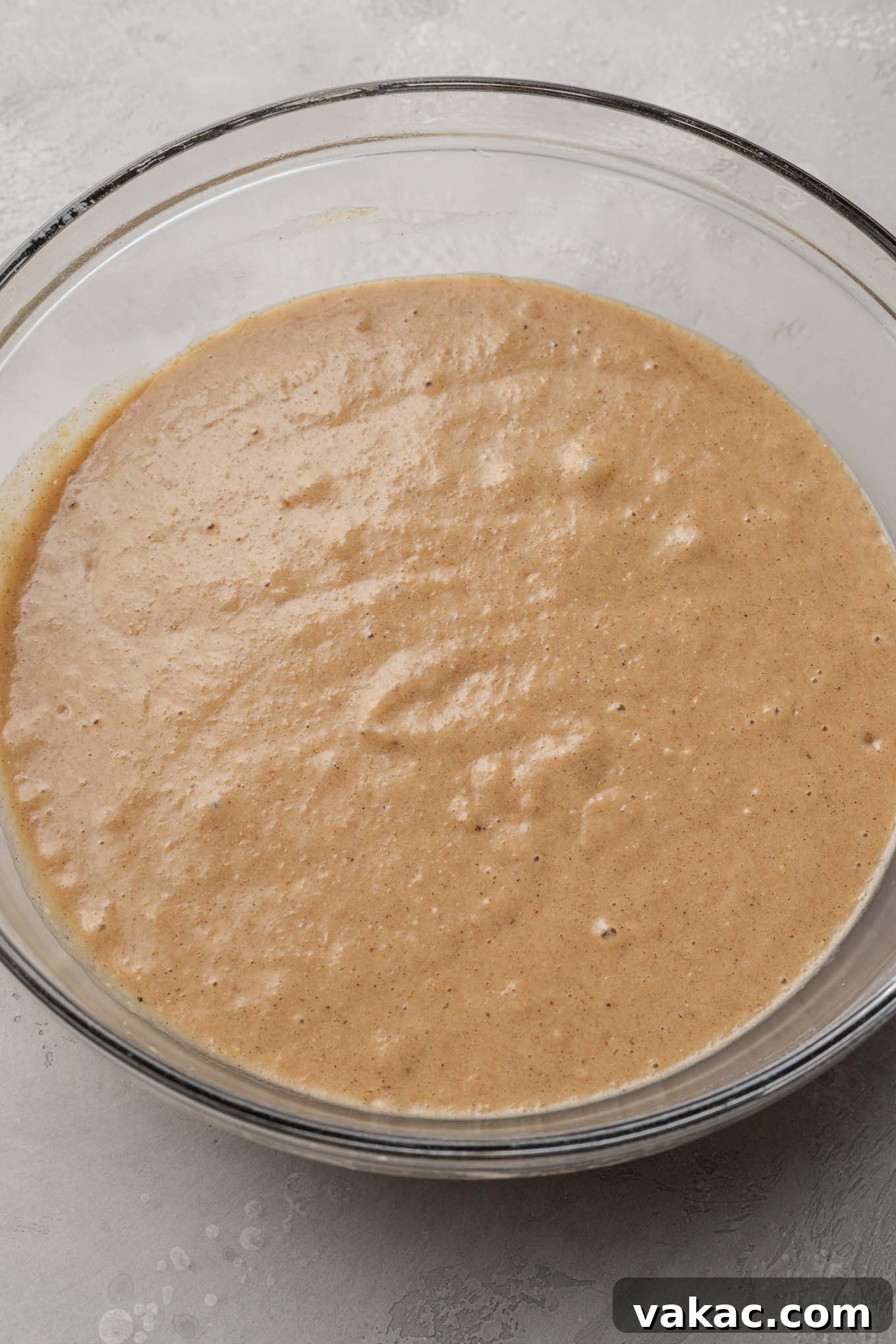 A beautifully textured applesauce cake batter rests in a clear glass mixing bowl, photographed from above, showcasing its readiness for baking.