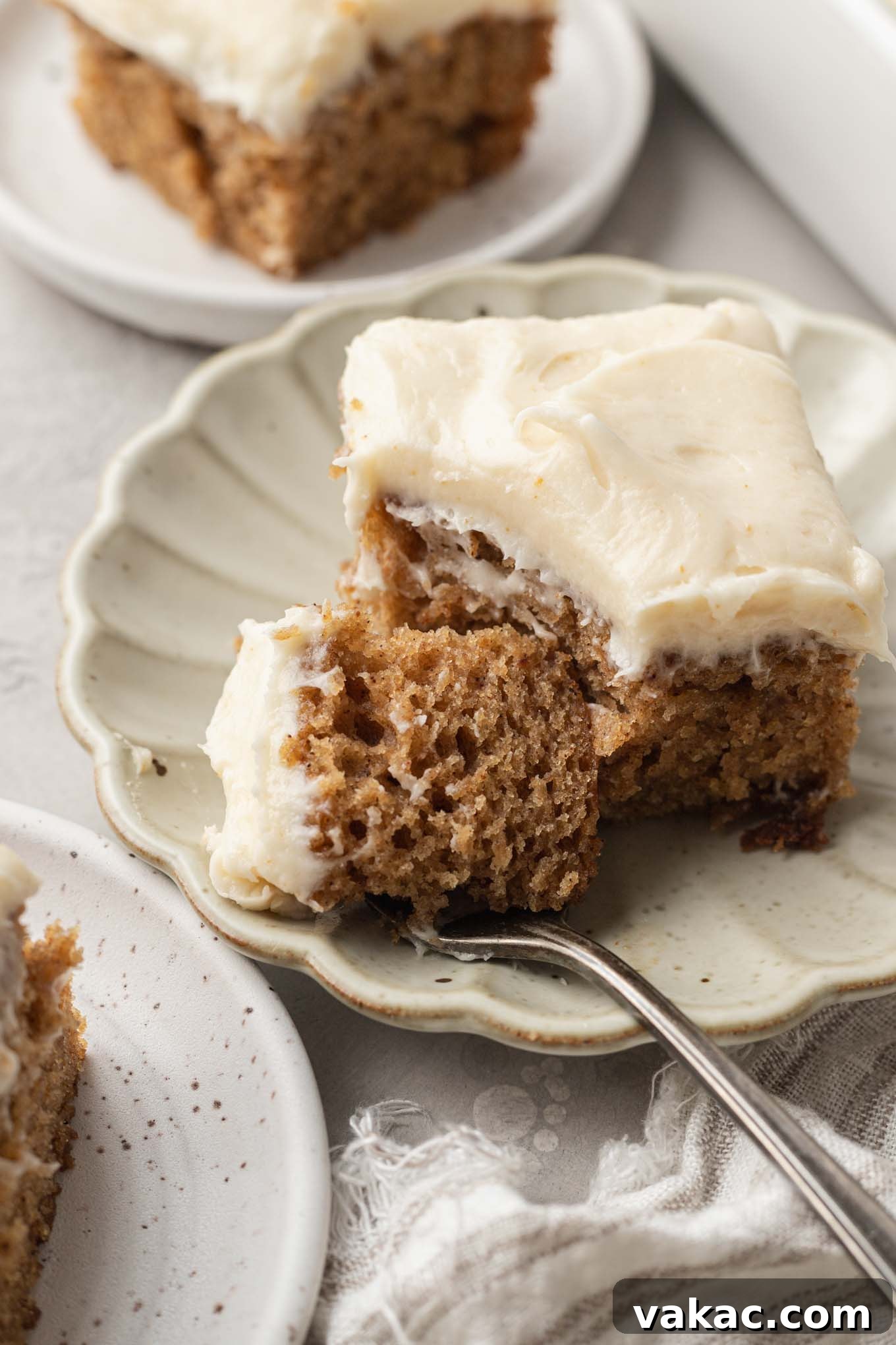 A delectable slice of applesauce cake adorned with creamy brown butter frosting, resting on a charming scalloped dessert plate, with a fork holding a perfect bite.
