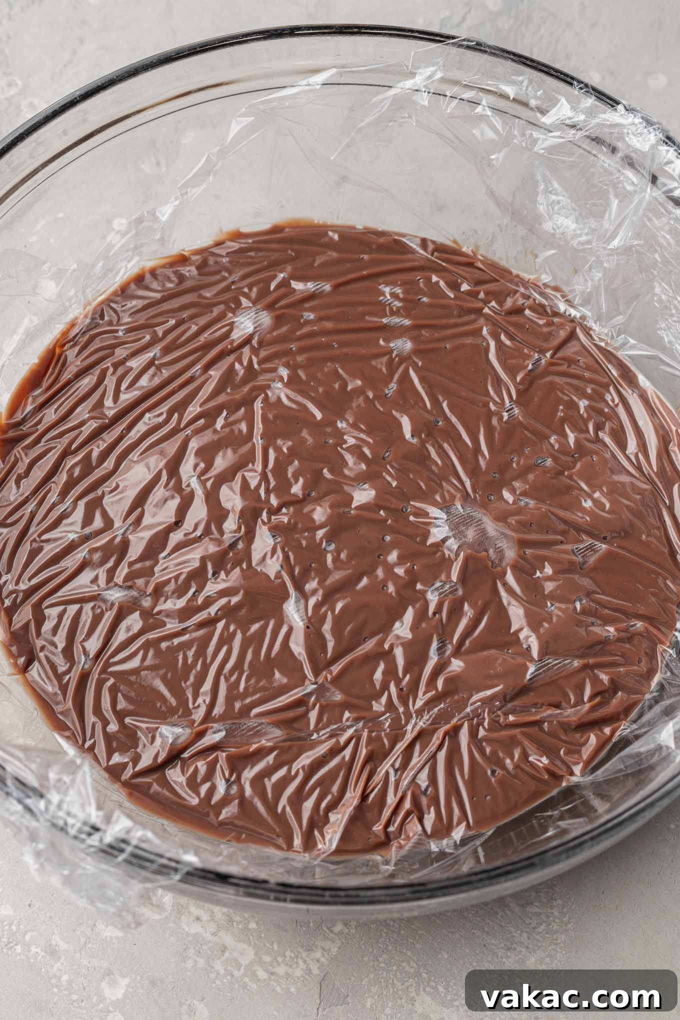 Sweet Soil Treats 5 An overhead view of homemade chocolate pudding cooling in a glass mixing bowl, covered directly with plastic wrap.