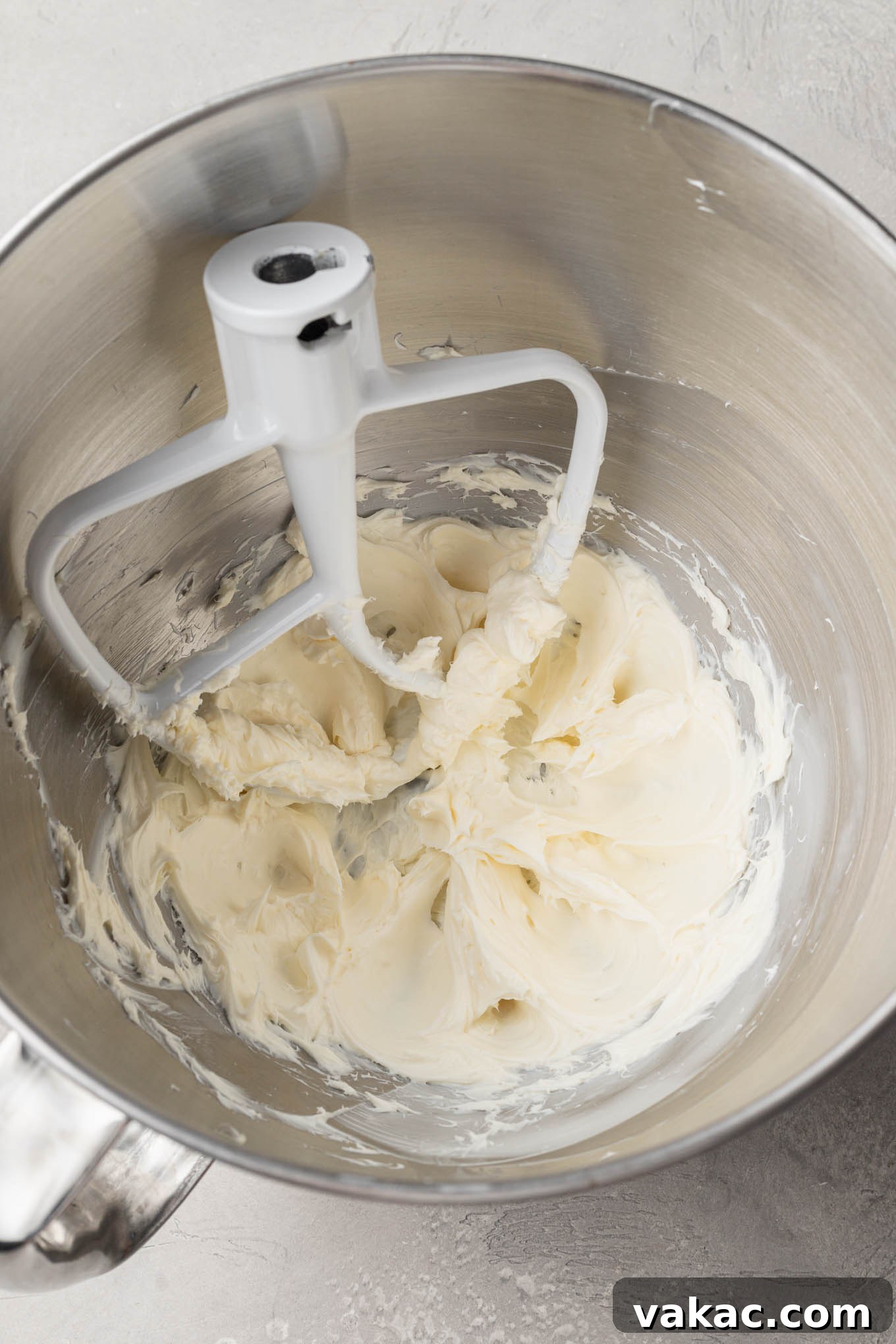 An overhead view of softened cream cheese and butter being beaten together in a mixing bowl using a paddle attachment, creating a smooth and creamy base.